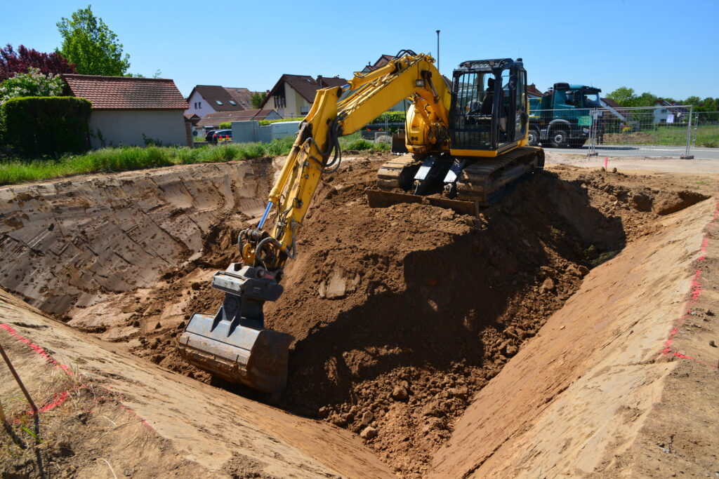 Bagger hebt auf einem Bauplatz im Neubaugebiet eine Baugrube aus